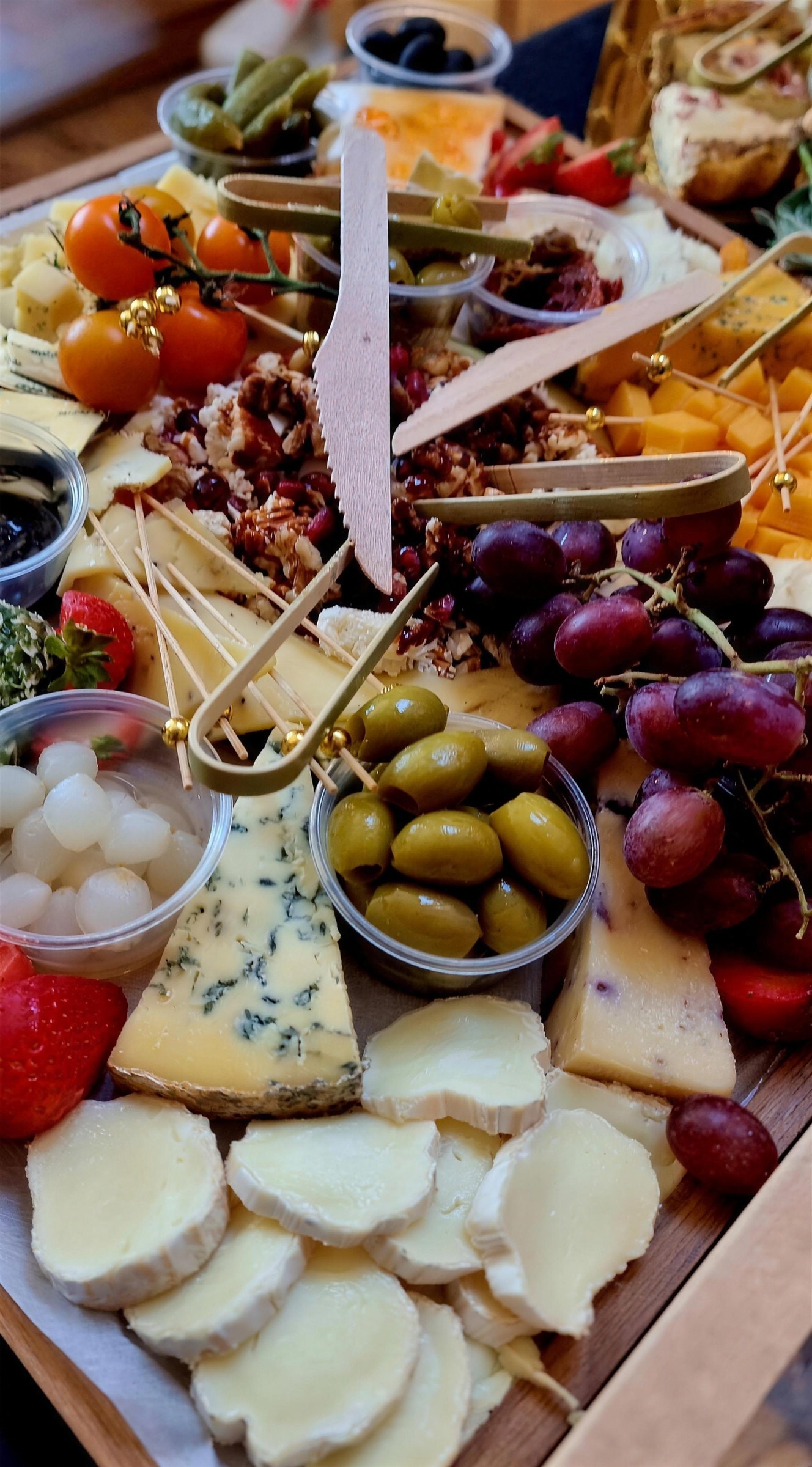 Close view of a cheese board with blue cheese, brie, grapes, olives, strawberries and pickles