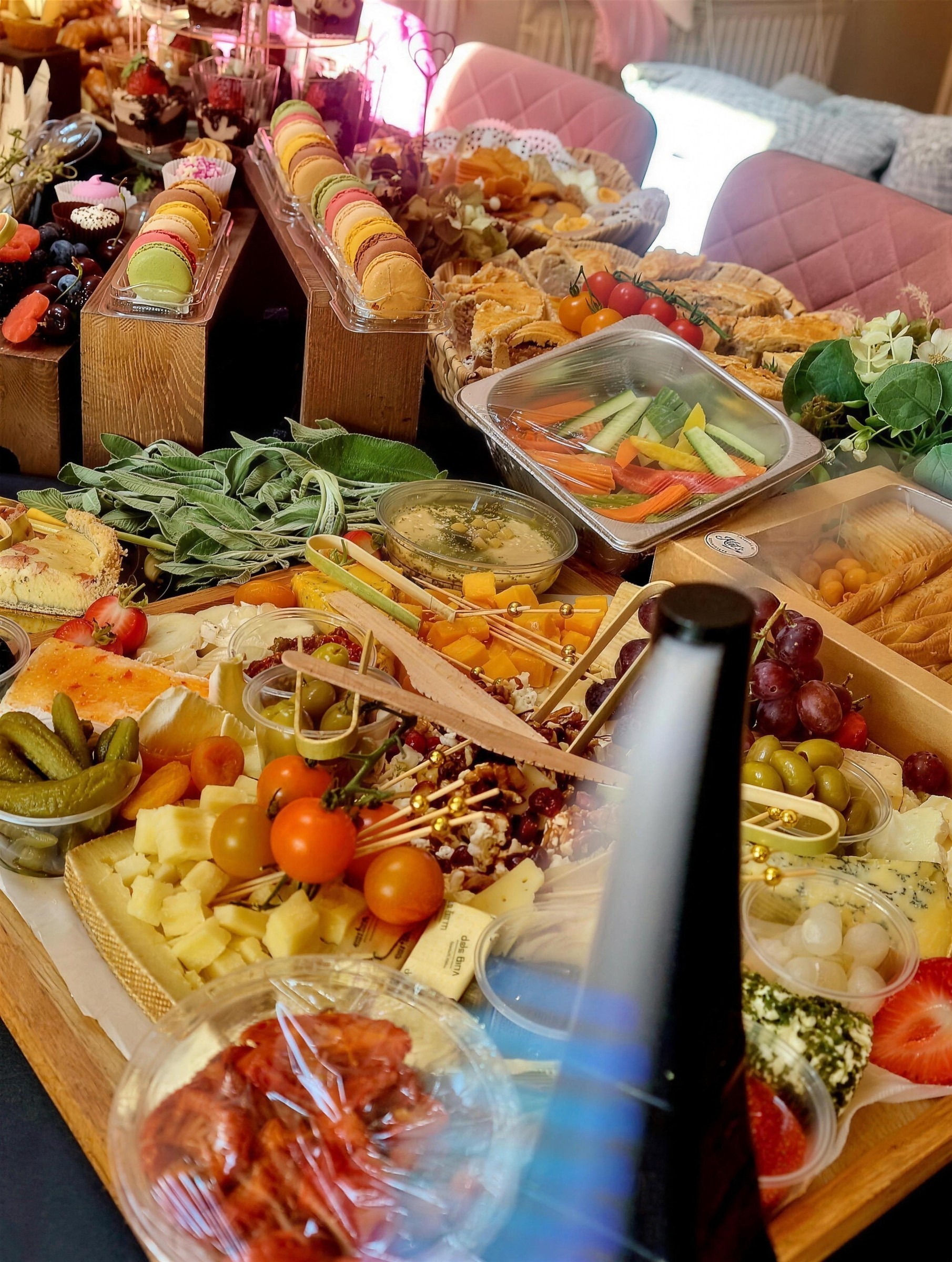 Grazing spread with macarons on wooden risers, quiche, cheese boards, fresh sage and crudités